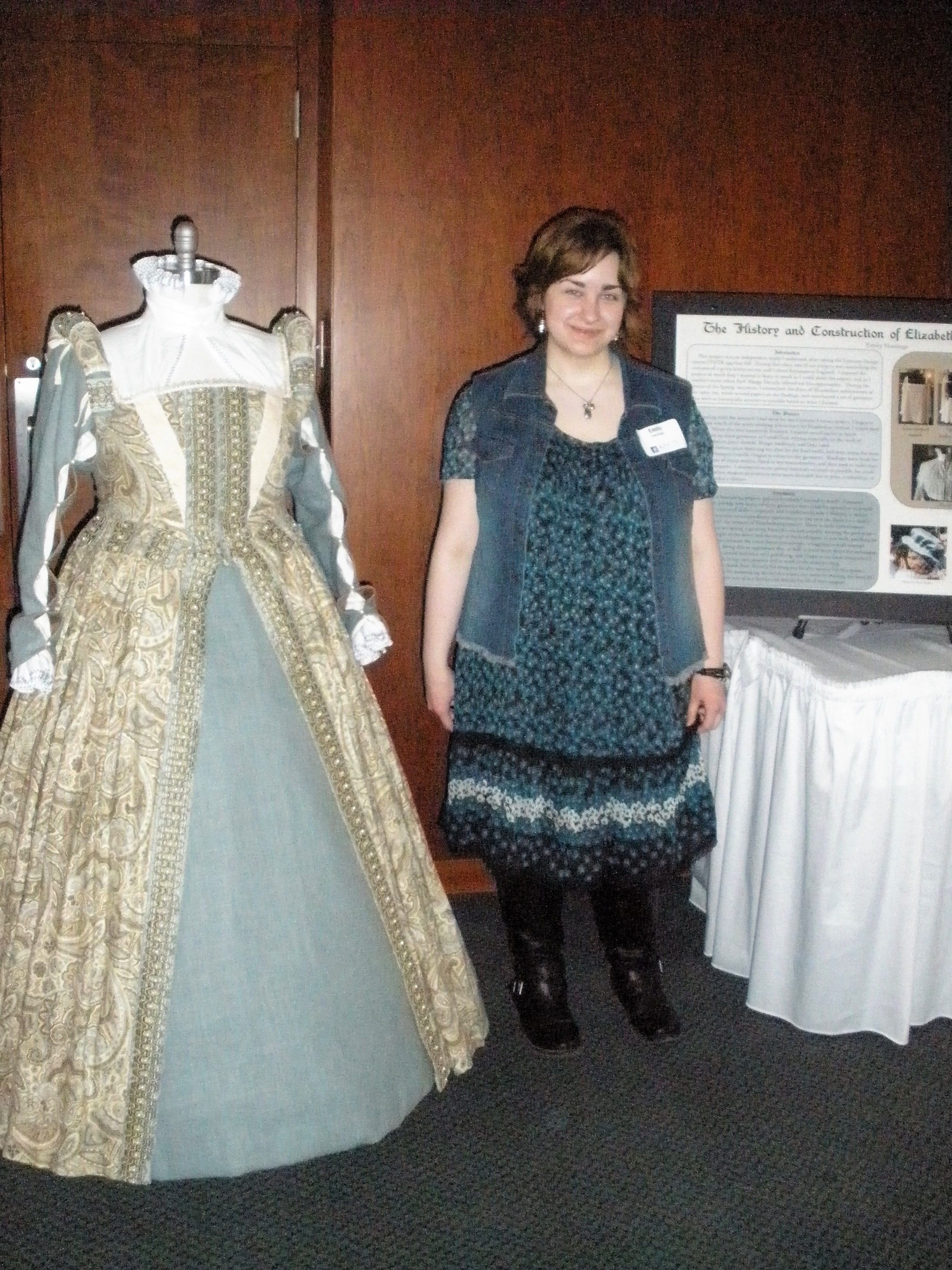 Emily stands by the gown and poster.