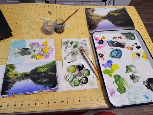 Paintings freshly finished on table surrounded by paint supplies.